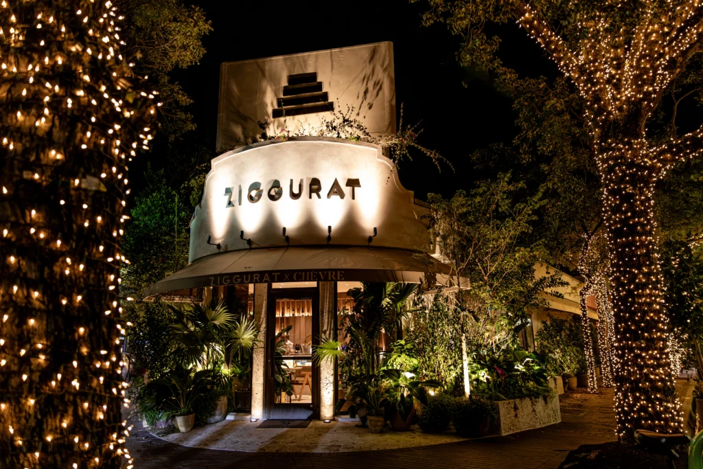 A warmly lit restaurant named Ziggurat with string lights wrapped around trees and greenery at the entrance, creating a cozy nighttime ambiance.